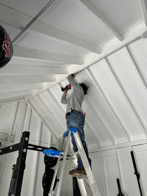 JFX Lighting installer on a ladder mounting a fixture on a white vaulted ceiling