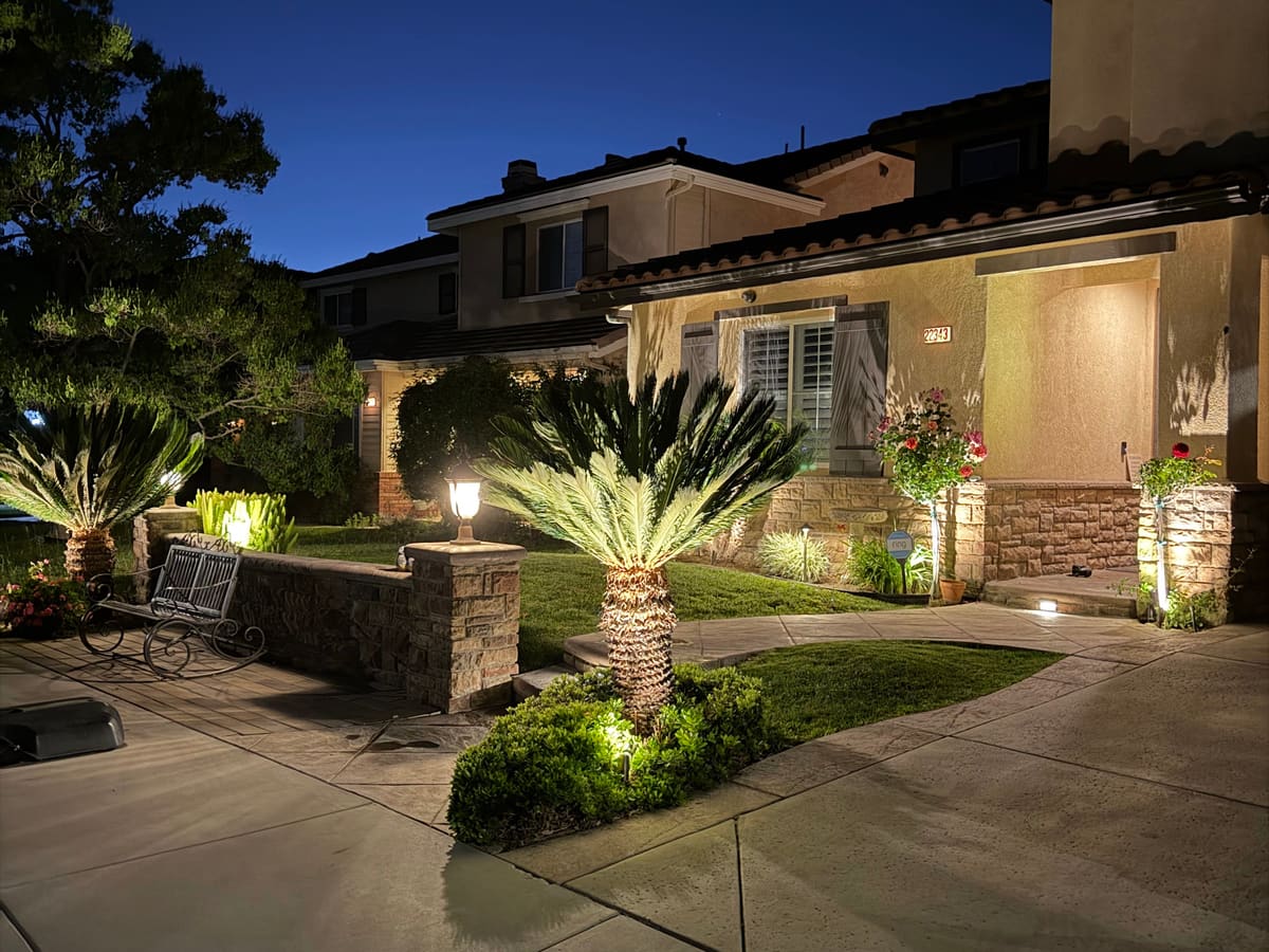 Front yard at dusk with landscape lighting on palms, planters and the entry of a two-story home