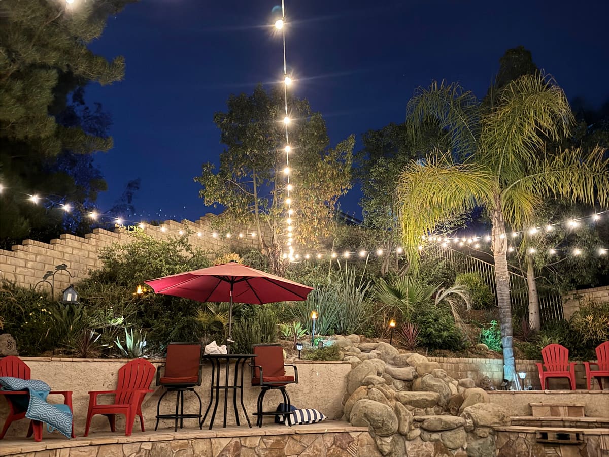 Backyard patio and pool at night under strands of warm string lights
