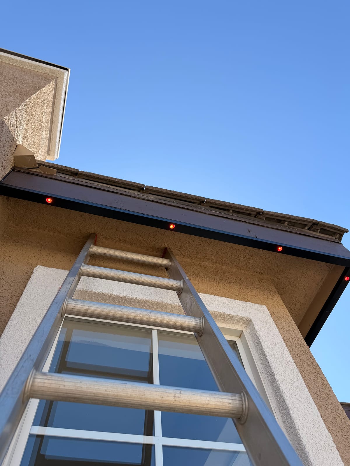 Permanent lights glowing red inside a fascia track during a JFX install, with a ladder against the home