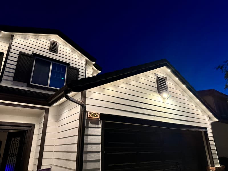 White two-story home at night with lights tucked under the roofline