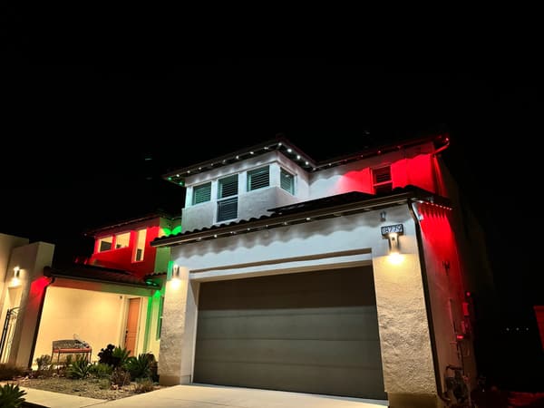 Two-story home at night with the permanent eave lights set to red and green for Christmas