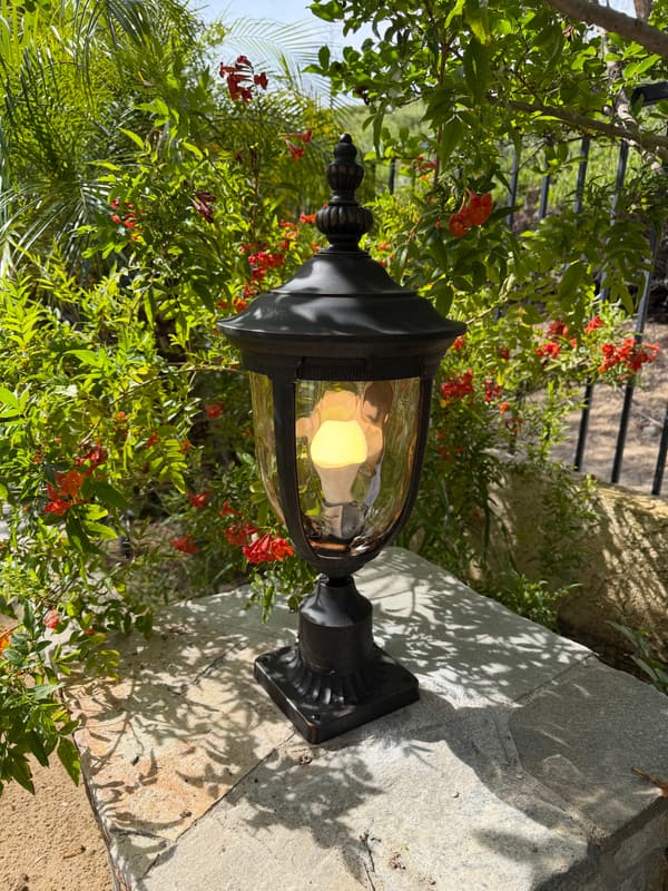 Black post-top lantern with a warm bulb on a stone ledge among red flowers