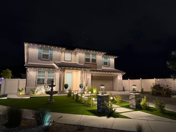 Two-story home at night with path lights along the front walk, a lit fountain and white roofline lights