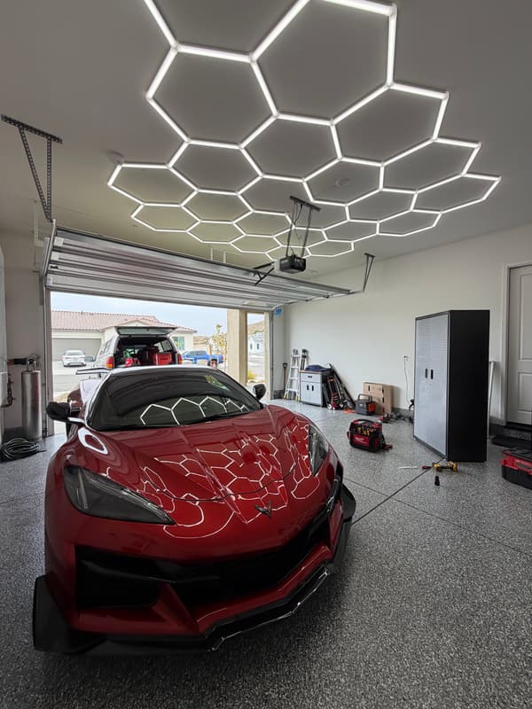 Red sports car parked in a garage under a hexagon LED ceiling grid
