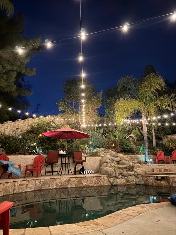 Backyard patio and pool at night under strands of warm string lights