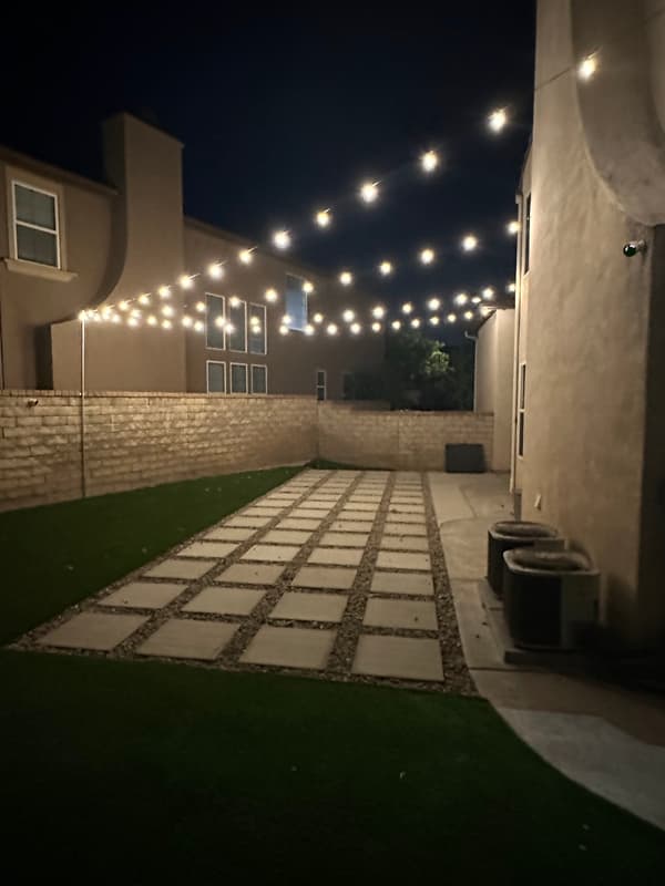 Side yard with paver path under rows of string lights at night