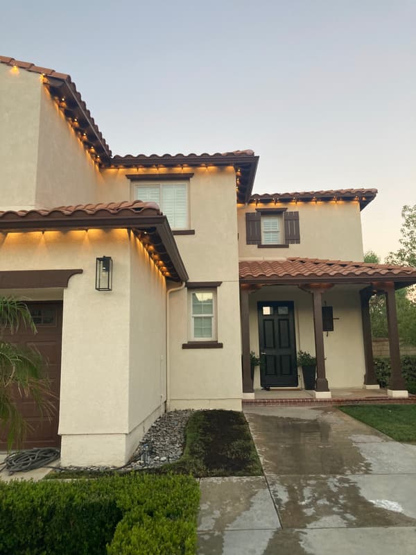 Stucco home with tile roof and warm roofline lights at dusk