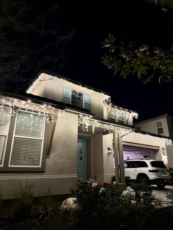 Two-story home with white icicle-style holiday lights along the roofline