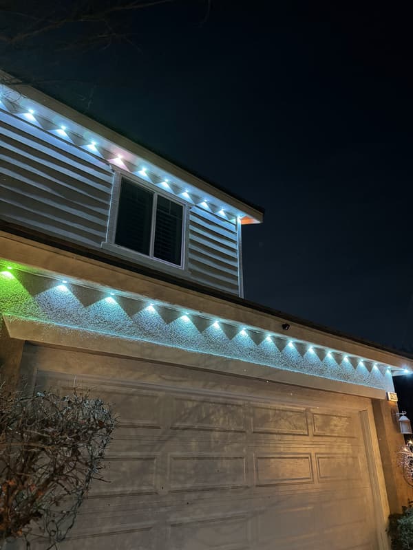 Close-up of permanent eave lights glowing white, blue and green along a roofline above a garage