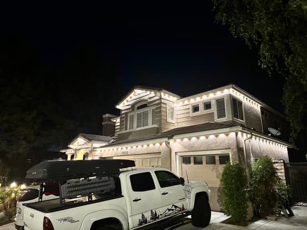 Two-story home at night with warm white roofline lights and a white pickup truck in the driveway