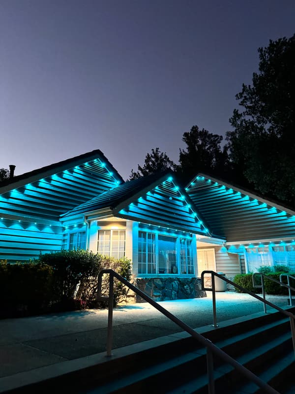 Single-story home lit in teal permanent eave lights at dusk, seen from the front steps
