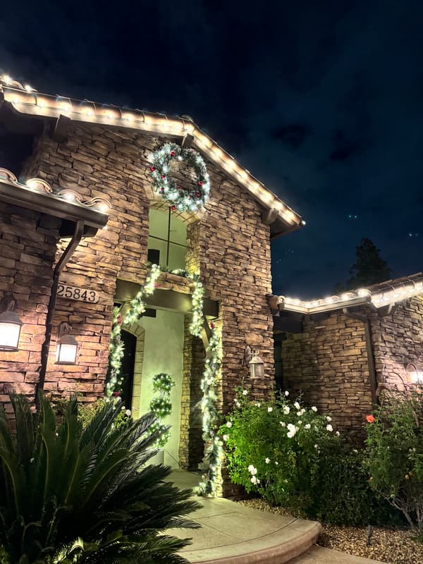 Stacked-stone entry with a wreath and garland, warm white lights along the rooflines at night
