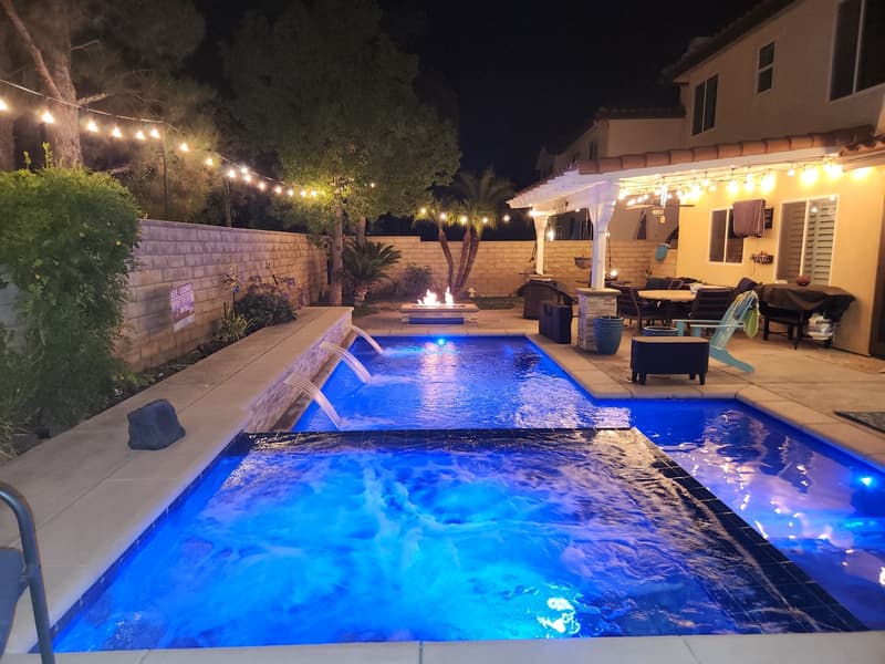Backyard pool and covered patio at night under warm string lights