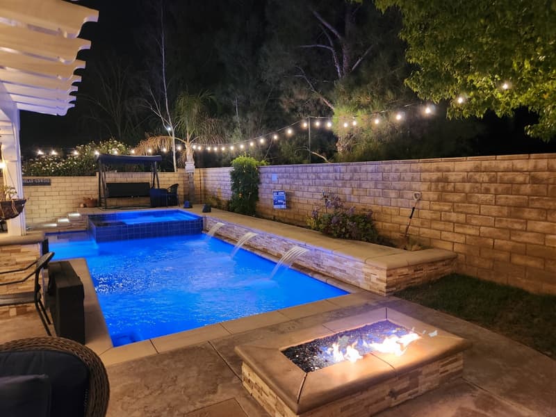 Pool with water features and a fire pit under strands of string lights